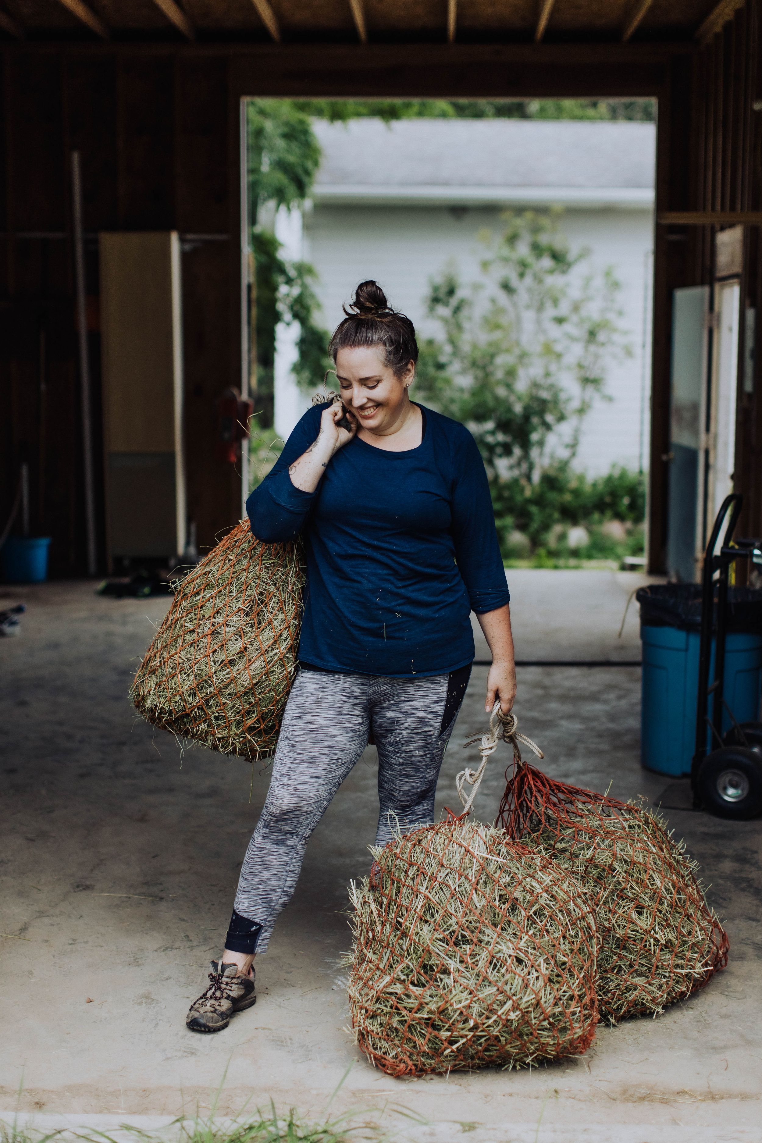 Person moving hay bales in a barn while wearing casual workout attire.