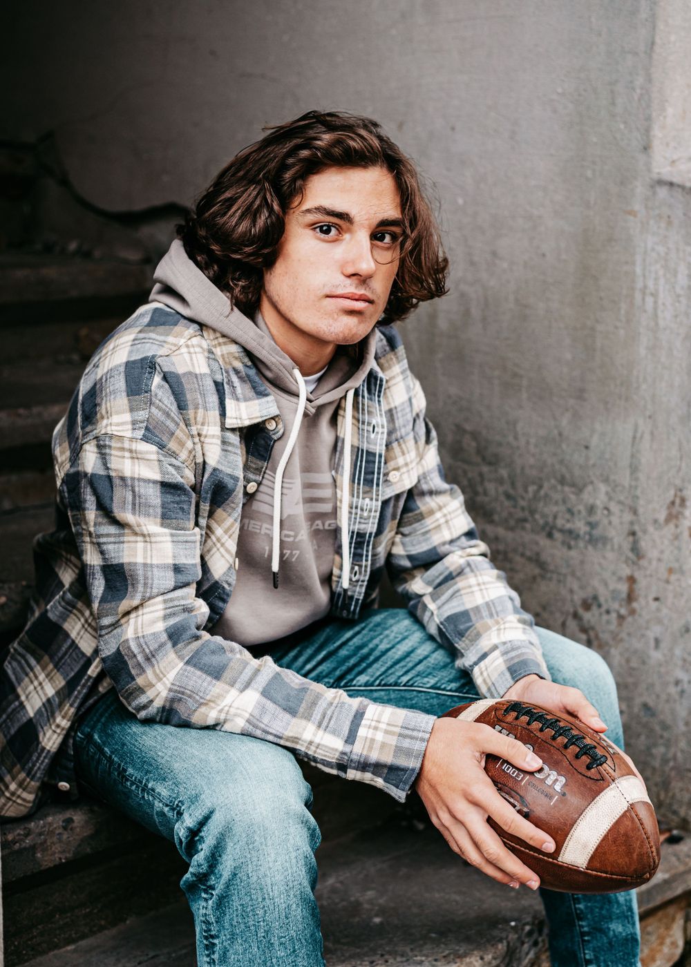 A casual portrait on concrete steps featuring plaid shirt, hoodie and football.