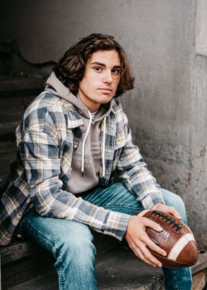 A casual portrait on concrete steps featuring plaid shirt, hoodie and football.