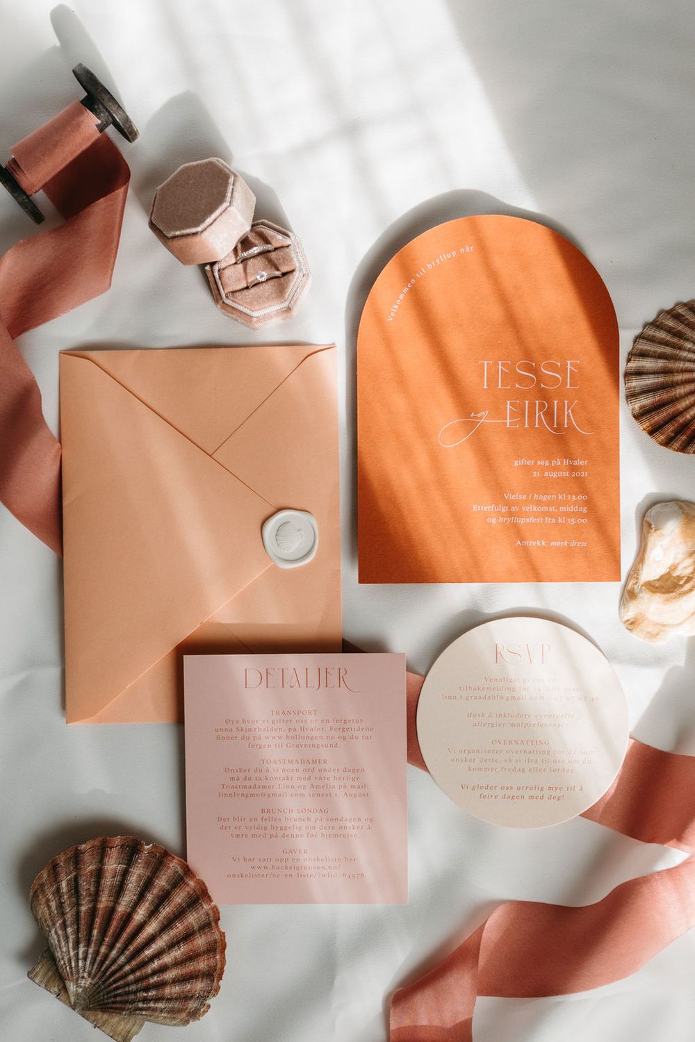 Peach colored wedding invitation suite with seashells and ribbons arranged in flat lay style.