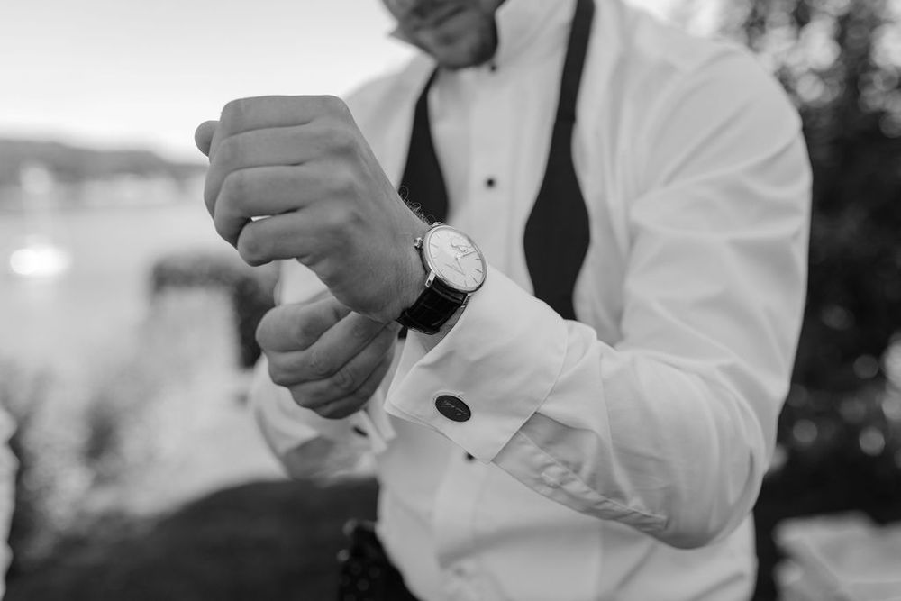 Black and white detail shot of a groom adjusting his watch while wearing a tuxedo.