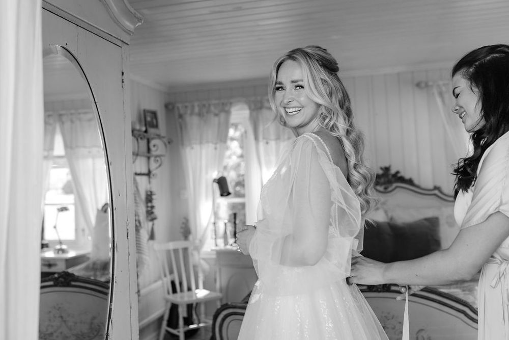 Black and white photo of bride getting ready in sunlit room with vintage decor.