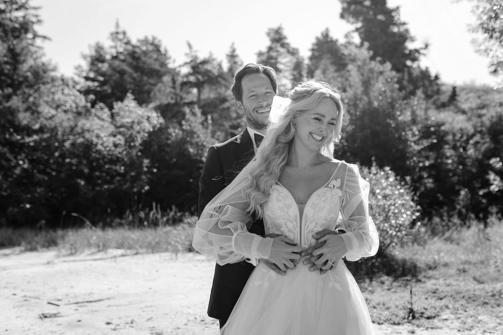 Black and white wedding photo showing tender moment between newlyweds outdoors.