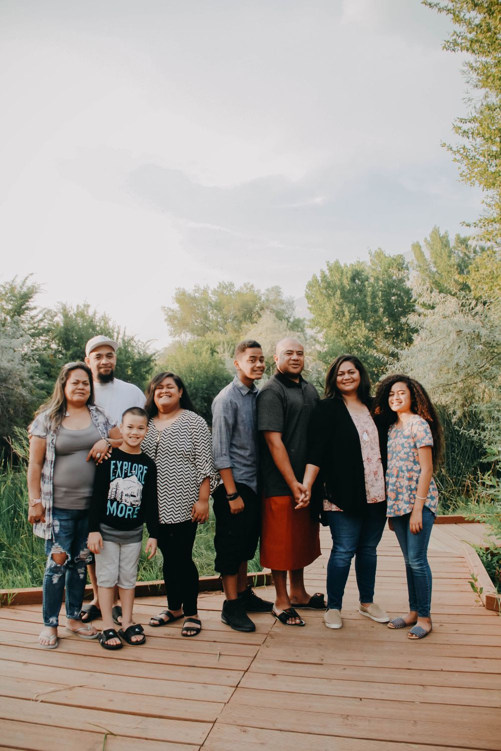 A multigenerational family of eight stands together on a wooden boardwalk surrounded by nature.