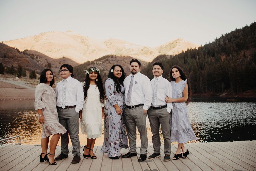 Family of seven smiling together on a dock with golden mountain sunset behind them.