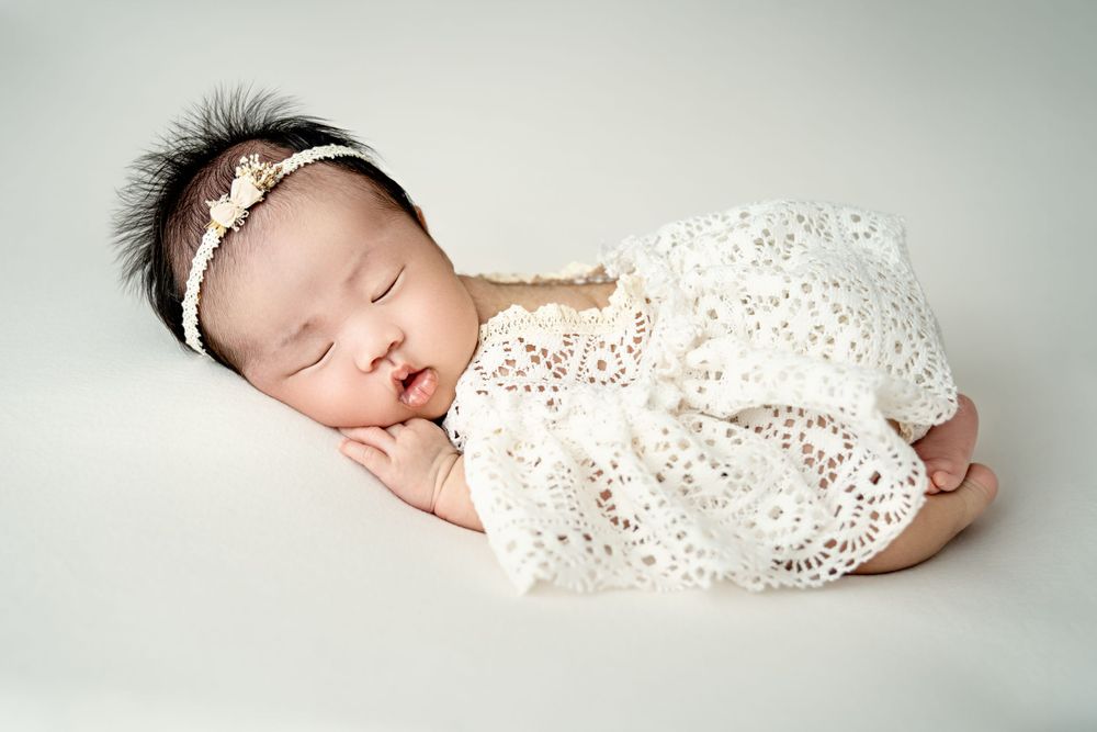 Classic newborn portrait in white lace wrap against light neutral backdrop.