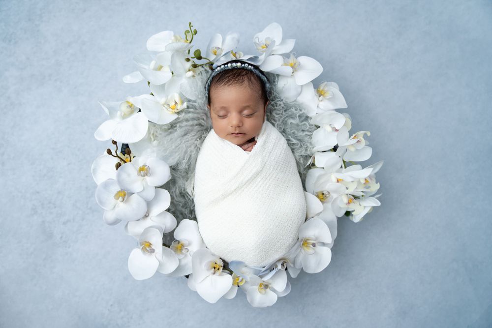 Elegant newborn photography with white orchids and soft blue background.