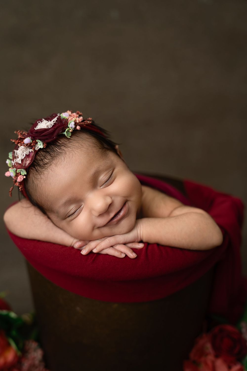 Artistic newborn portraits on burgundy cushion with delicate floral headpiece.