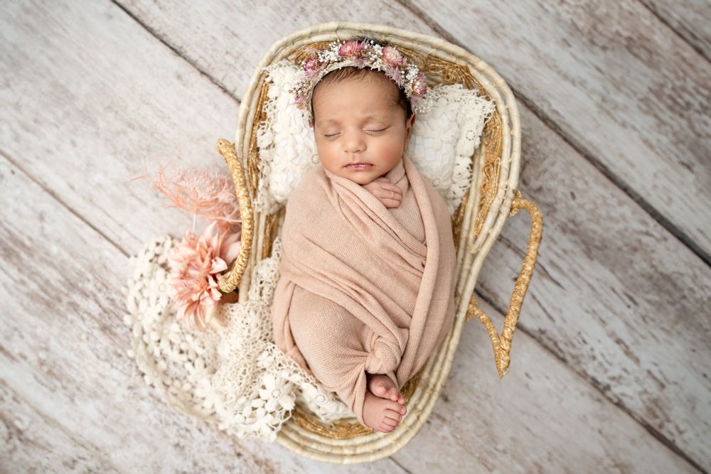 Delicate newborn portrait session with soft pink tones and vintage styling on whitewashed wood.
