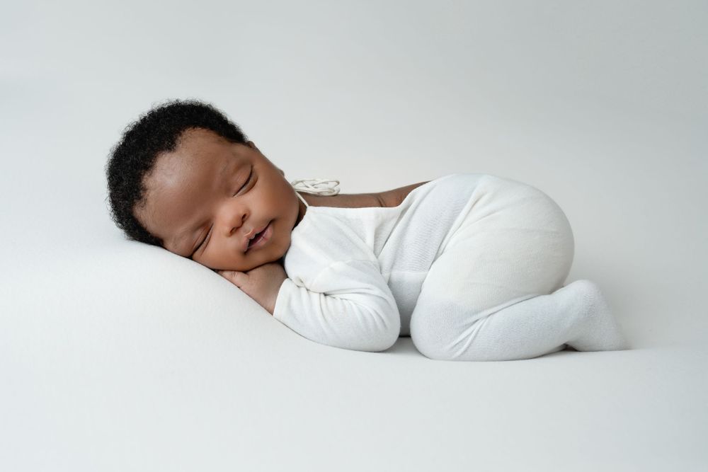 Minimalist newborn photography on clean white background with simple white outfit.