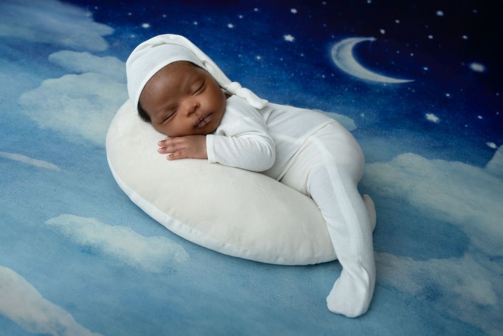 Dreamy nighttime themed newborn photo with stars and moon backdrop.
