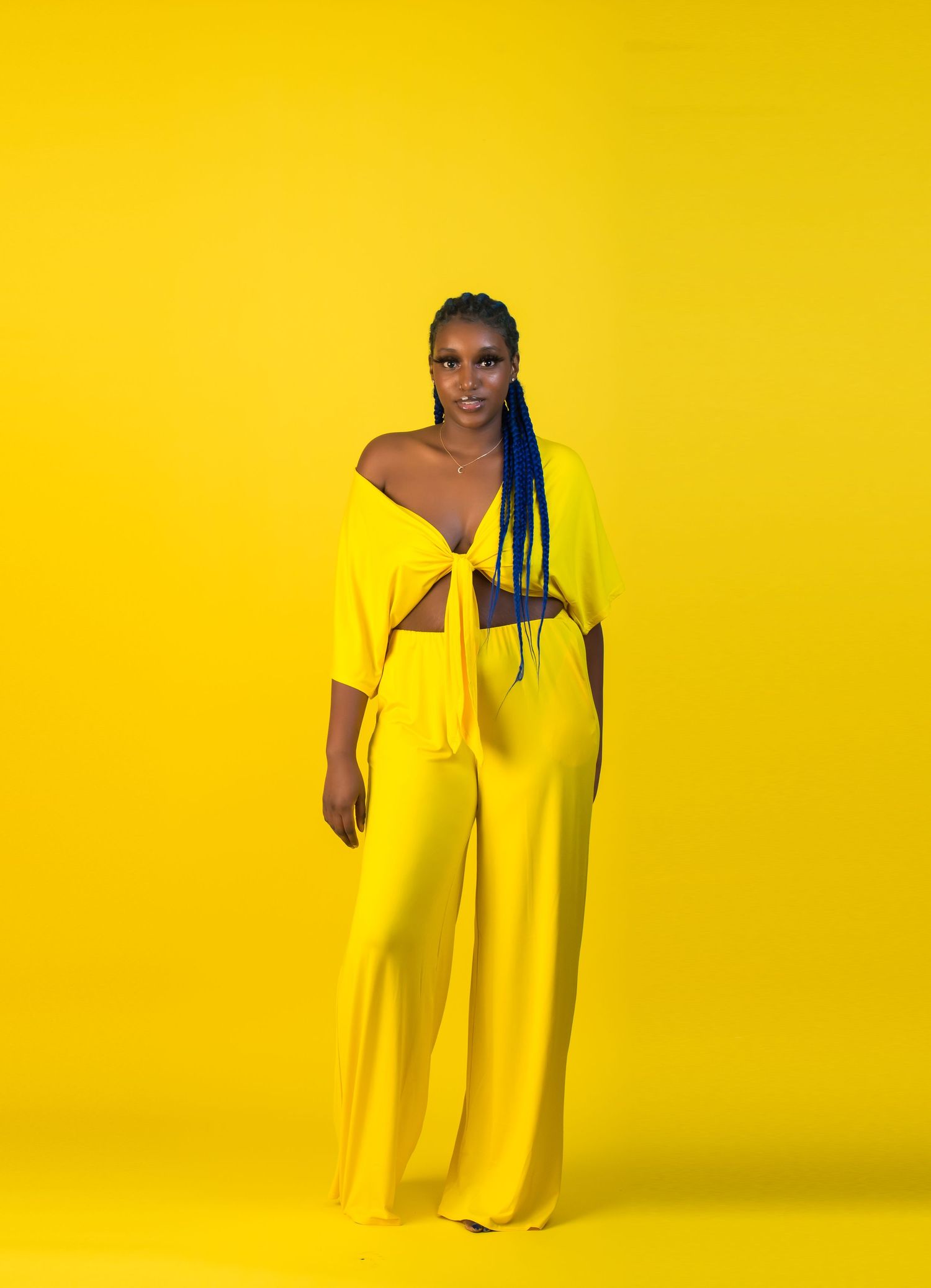 Fashion poses against vibrant yellow backdrop wearing flowing yellow dress.