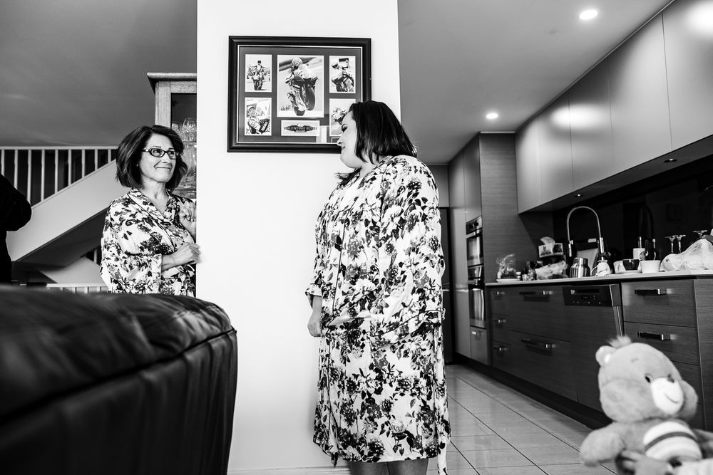 Black and white image showing reflections of florally dressed figures in a modern home interior.