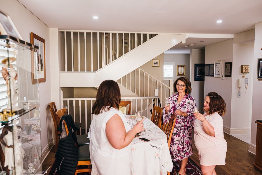A group gathers in a modern home interior with white walls and a staircase during preparations.