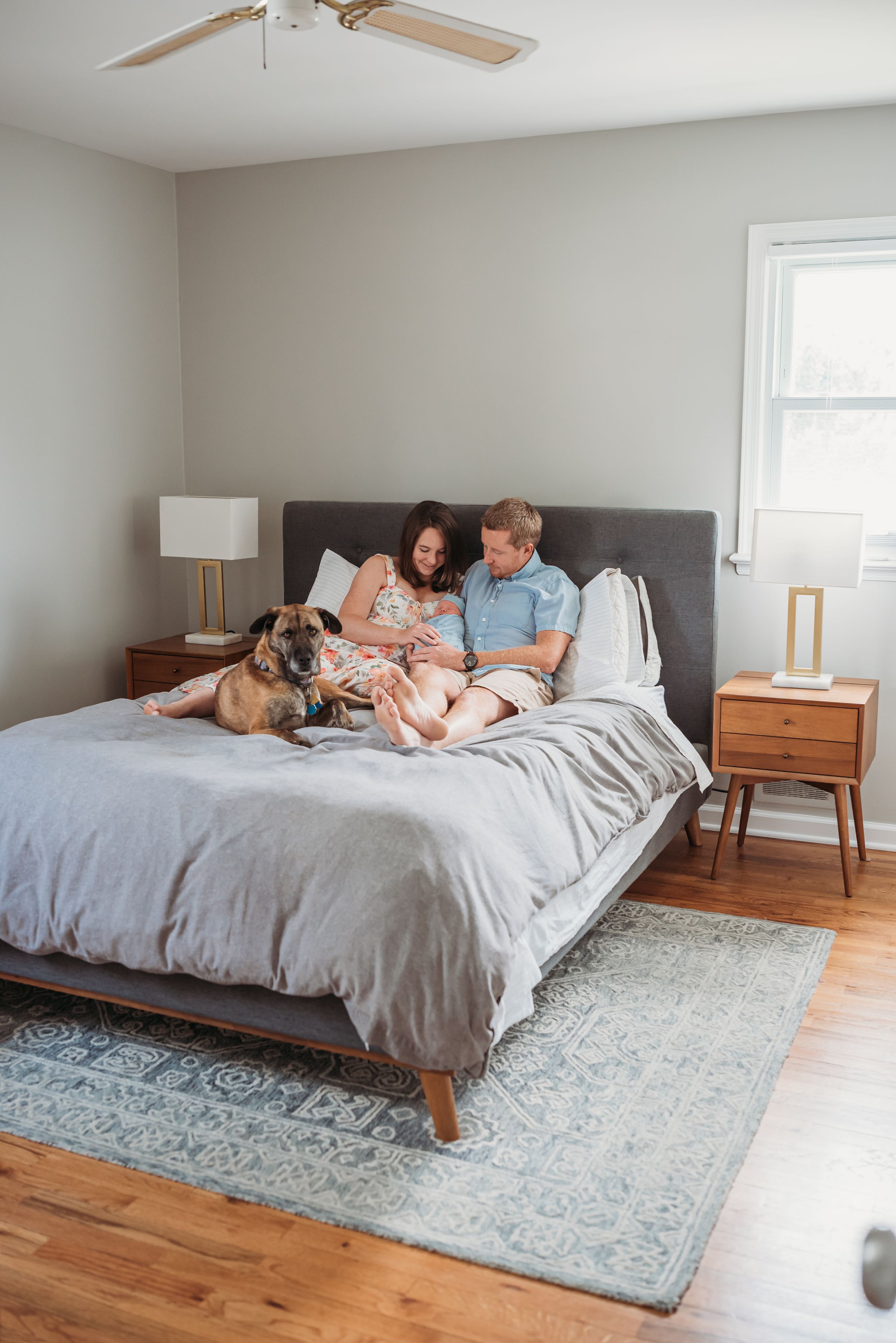Family with dog snuggles on master bed with their new baby boy.