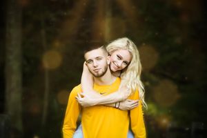 A couple embraces outdoors with a soft bokeh background during a photoshoot.
