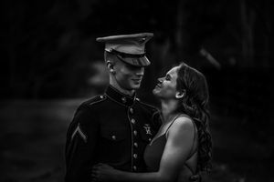 A Marine in dress uniform shares an intimate moment with his partner in a dramatic black and white photo.