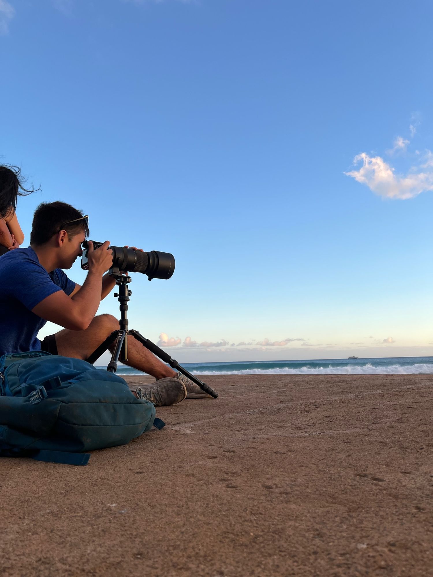 Photographer lying on beach sand capturing ocean waves with professional camera equipment.