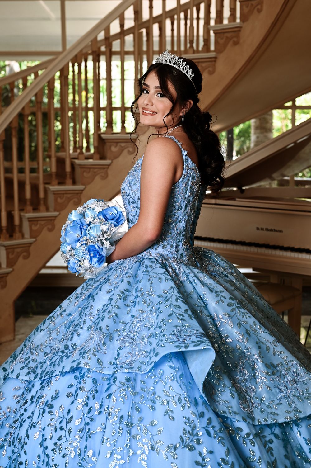 Stunning blue quinceañera dress with floral details photographed by a wooden staircase.