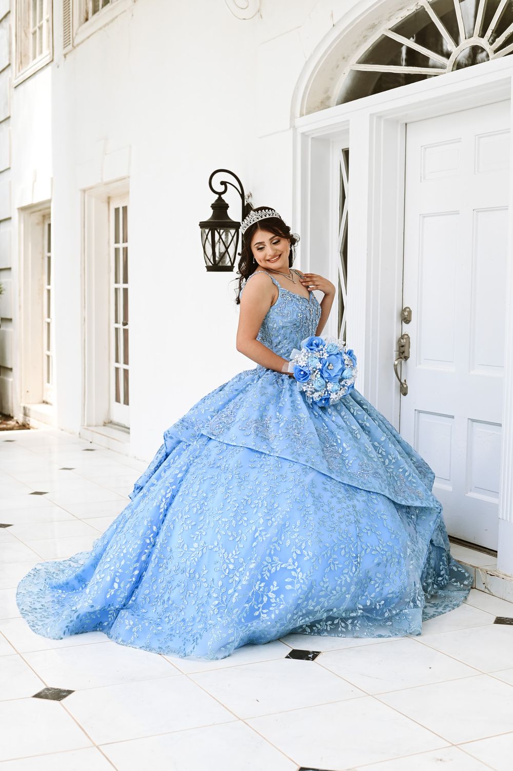 Light blue princess ball gown with lace detailing against classic white colonial architecture.