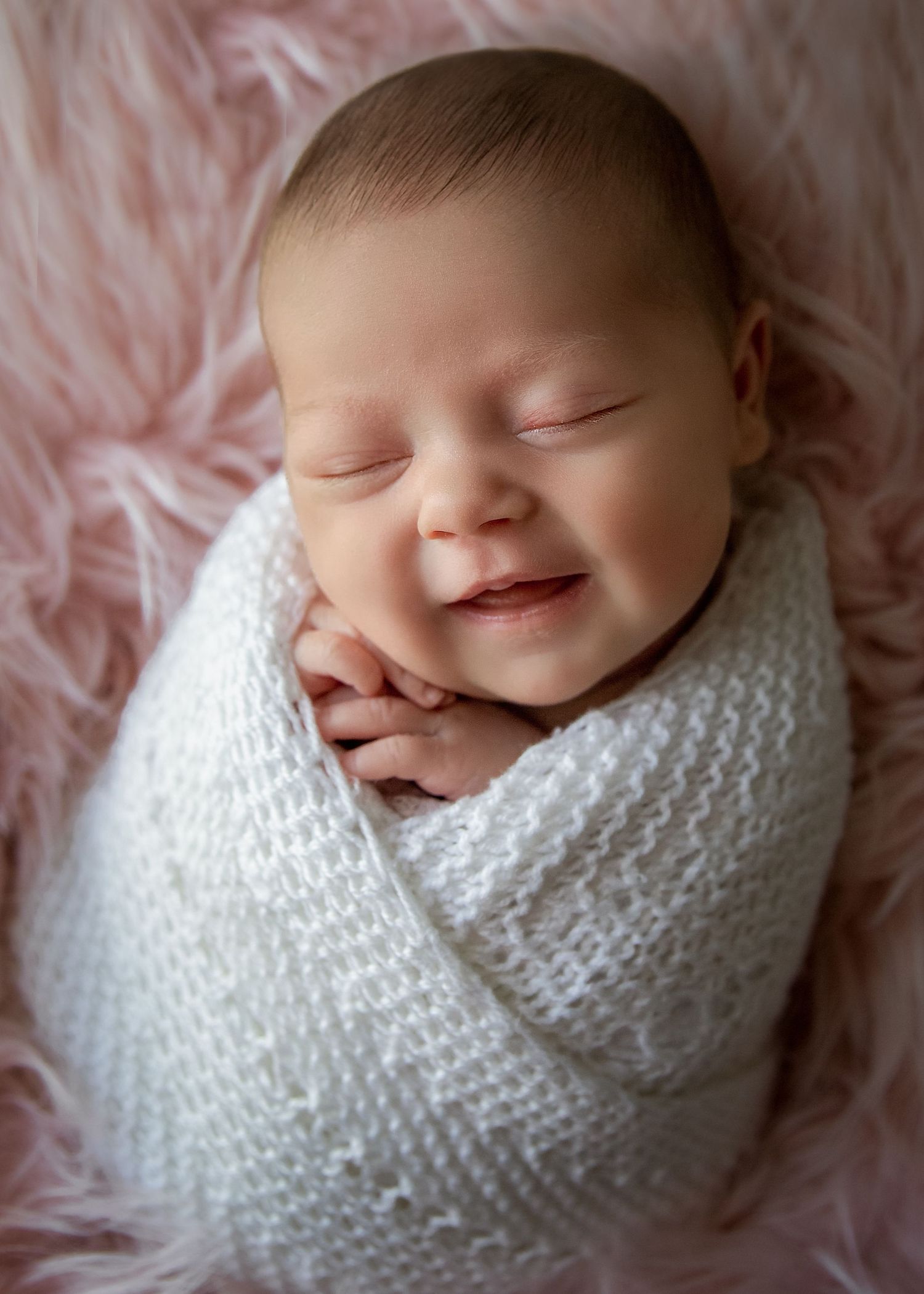 Wrapped baby girl on Flokati smiling for newborn photoshoot