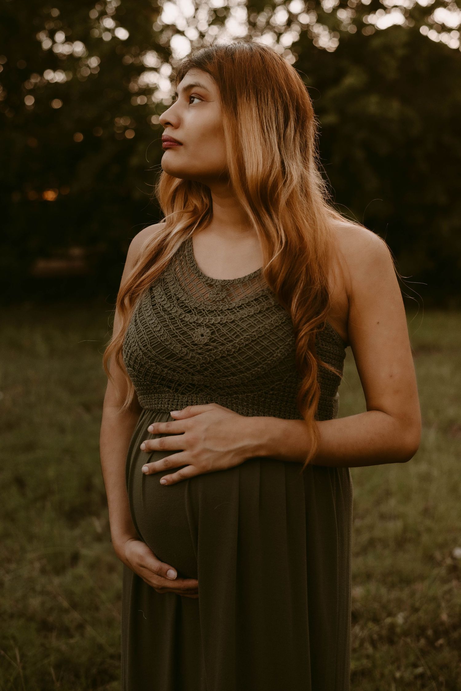 Side profile maternity portrait with olive dress and long flowing hair at sunset.