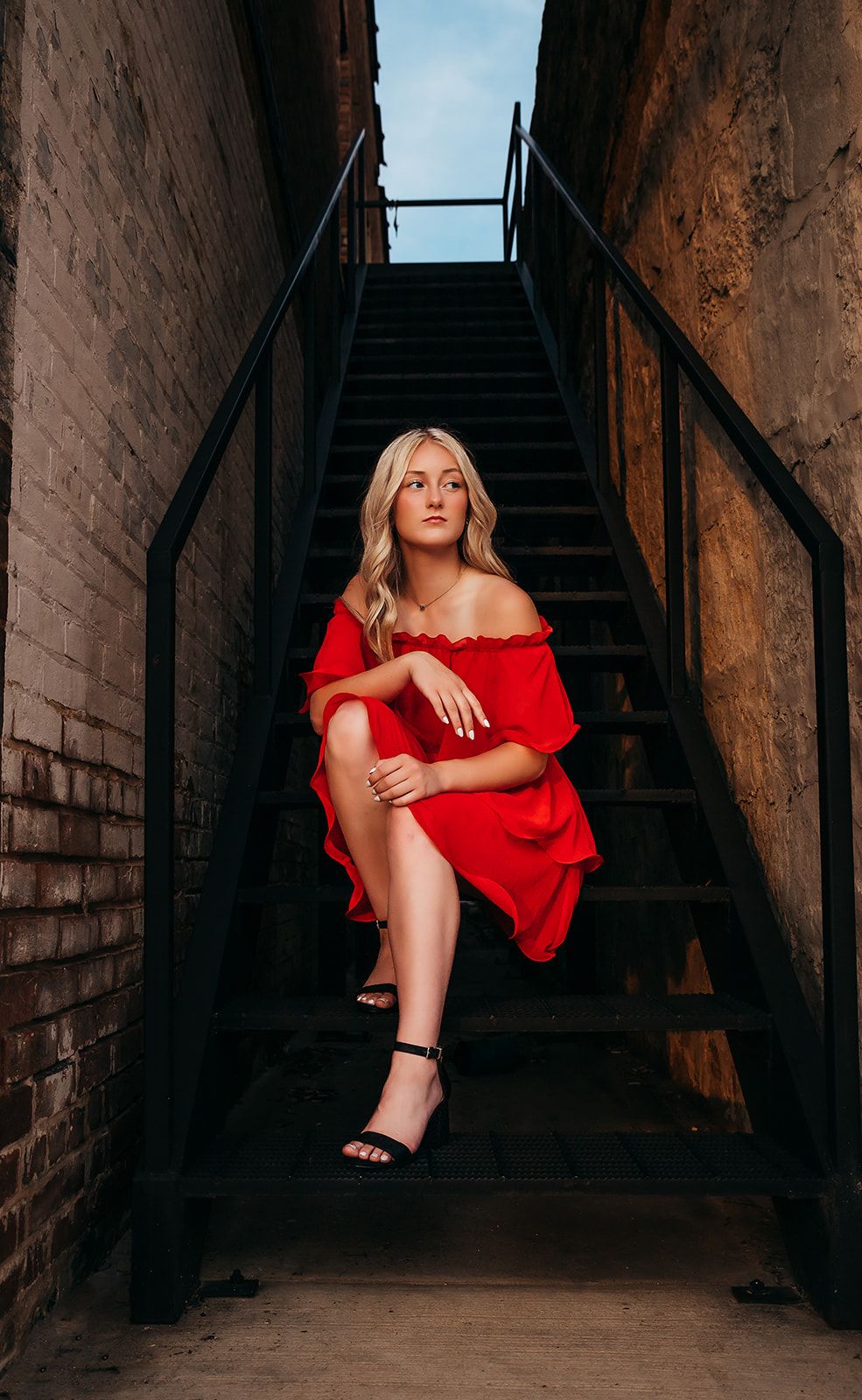 Woman in red dress poses dramatically on dark industrial stairwell.