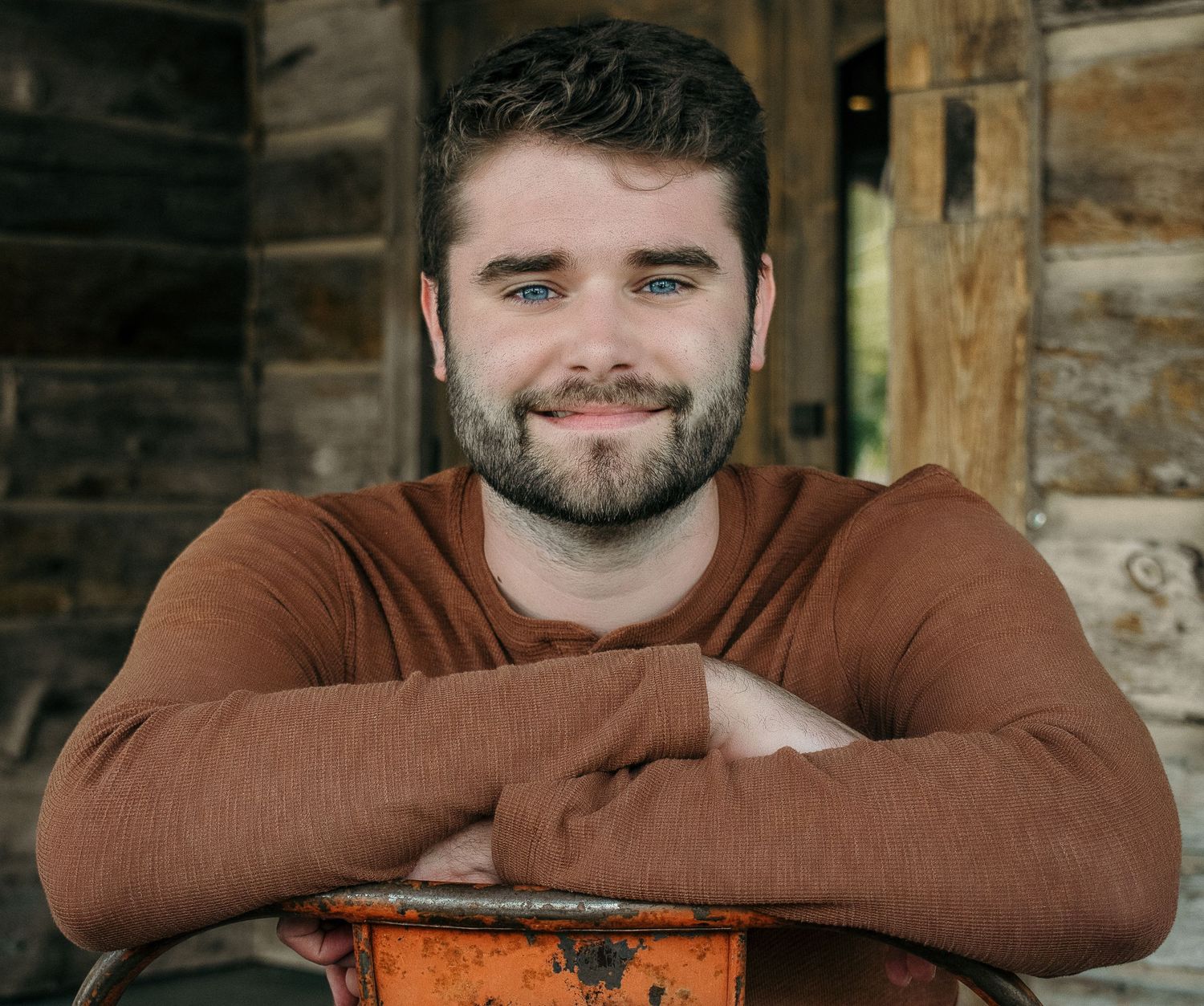 A relaxed portrait leaning on rustic wood wearing a brown henley shirt.