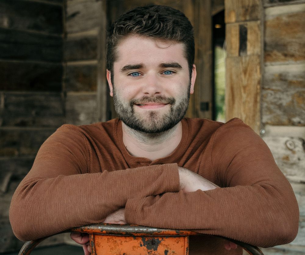 A relaxed portrait leaning on rustic wood wearing a brown henley shirt.