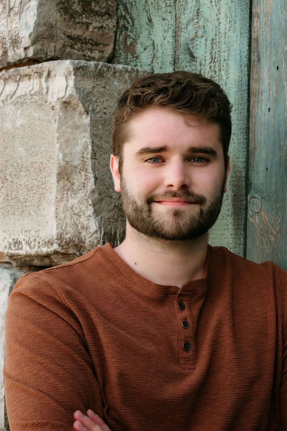 A casual outdoor portrait against weathered turquoise wood and stone wall.