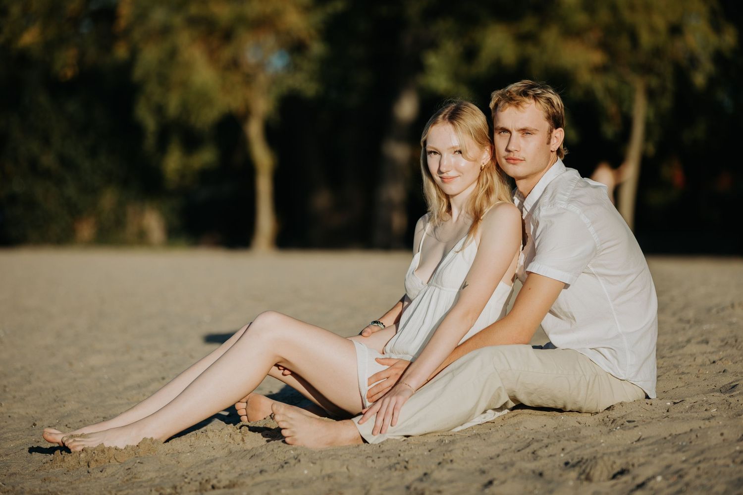 Couple sitting down at the beach looking straight at the camera