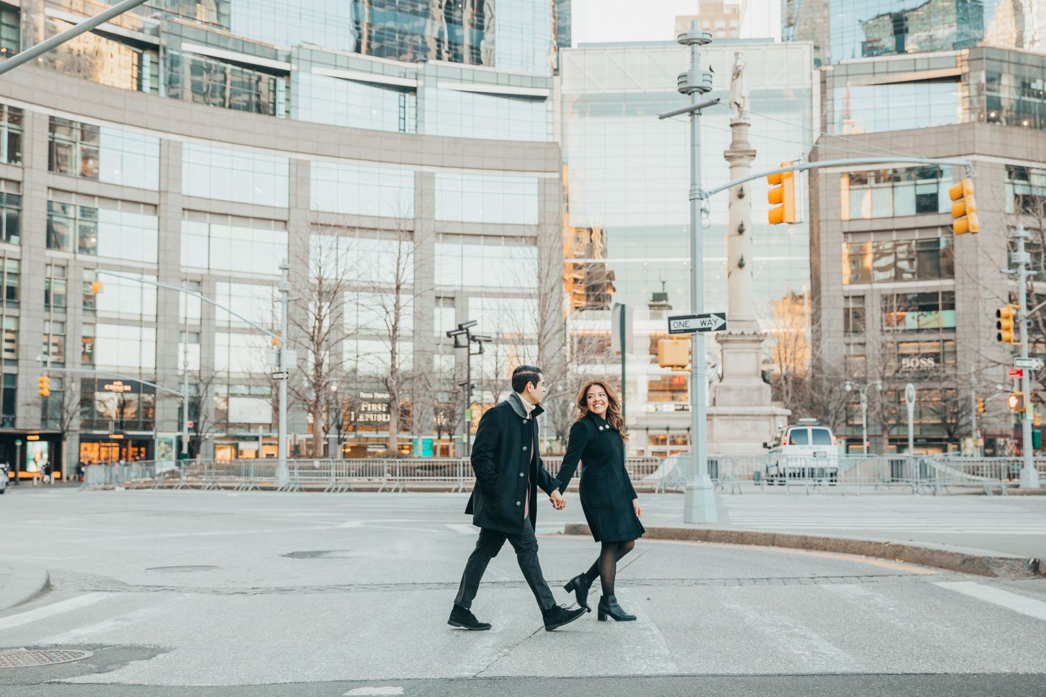 Couple holding hands while crossing a city street with glass buildings in background.