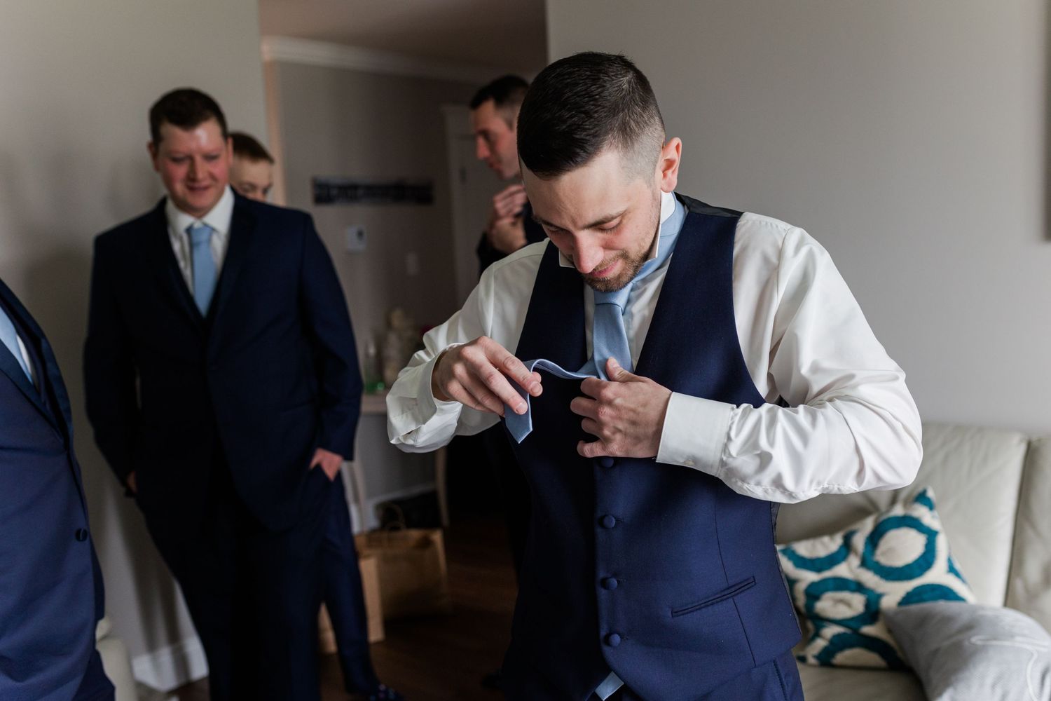 Wedding preparations show groomsmen helping with formal attire in a modern room.