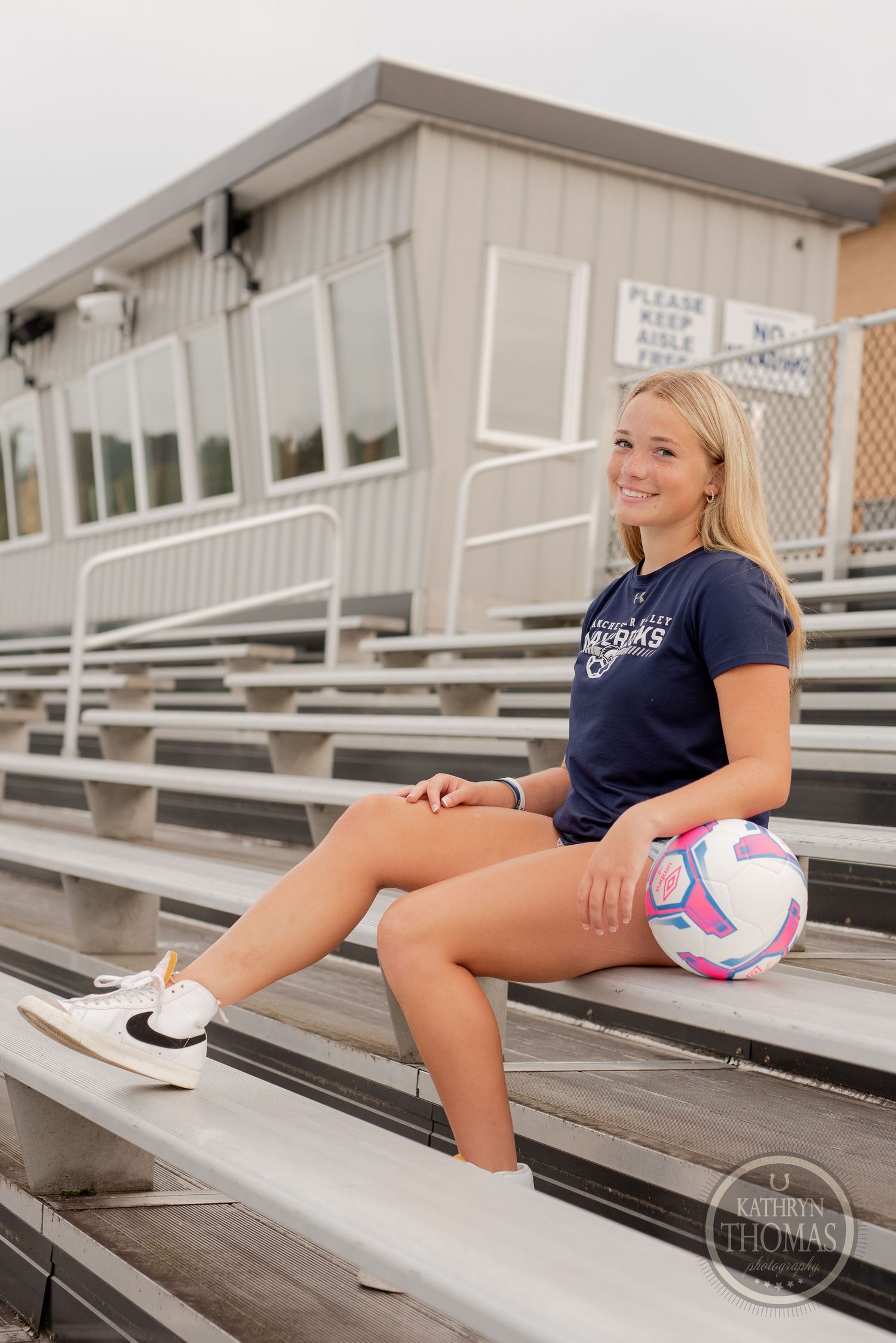 Soccer player sitting on metal bleachers with pink and white ball during team photo session.