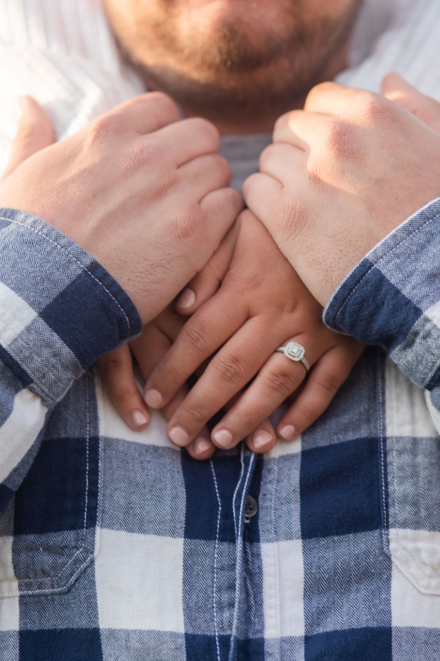 Close up of hands with an engagement ring wearing plaid flannel sleeves.