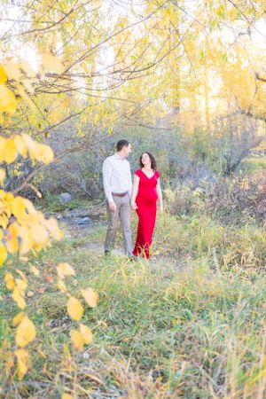 A couple's outdoor maternity photo amid yellow autumn leaves and natural scenery.
