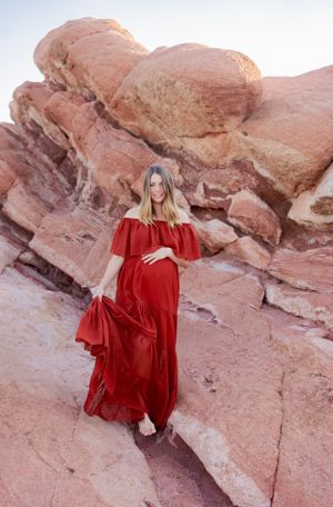 A flowing red maternity dress creates drama against layered red rock formations.