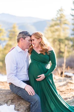 Romantic maternity portrait in green dress against mountain backdrop.