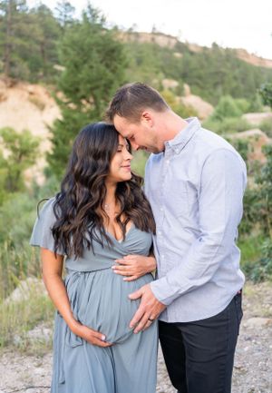 A tender maternity moment captured against a mountain backdrop in soft lighting.