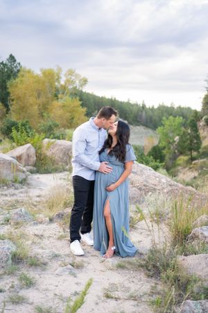 Couple embraces on rocky terrain with autumn trees and mountain views in the background.