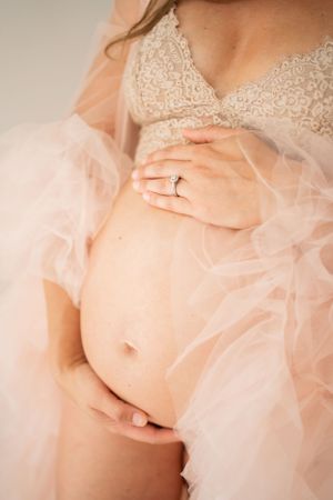 Close-up of pregnant belly with delicate lace and tulle overlay featuring engagement ring.