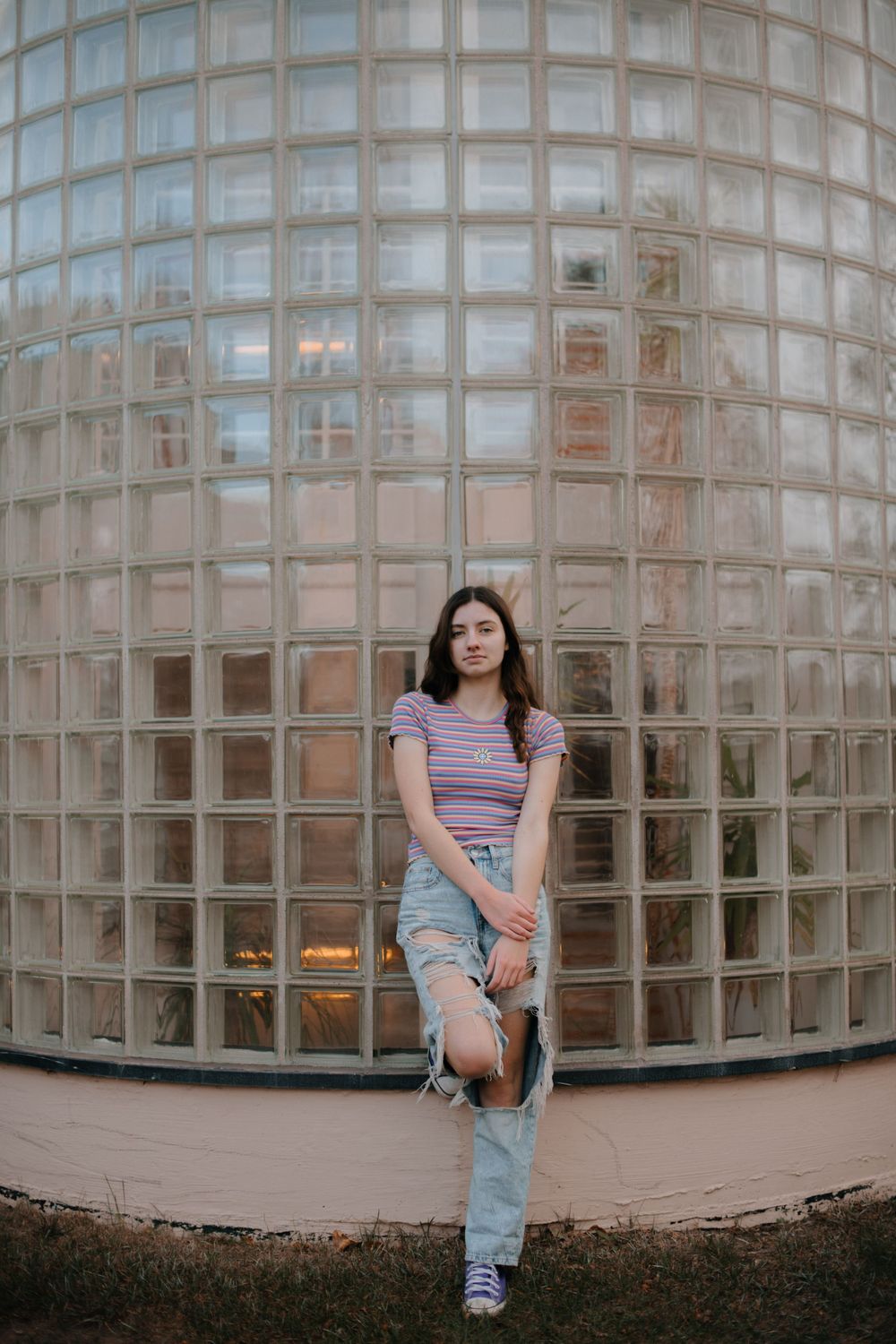 Fashion portrait against geometric glass block wall in casual striped top and distressed jeans.