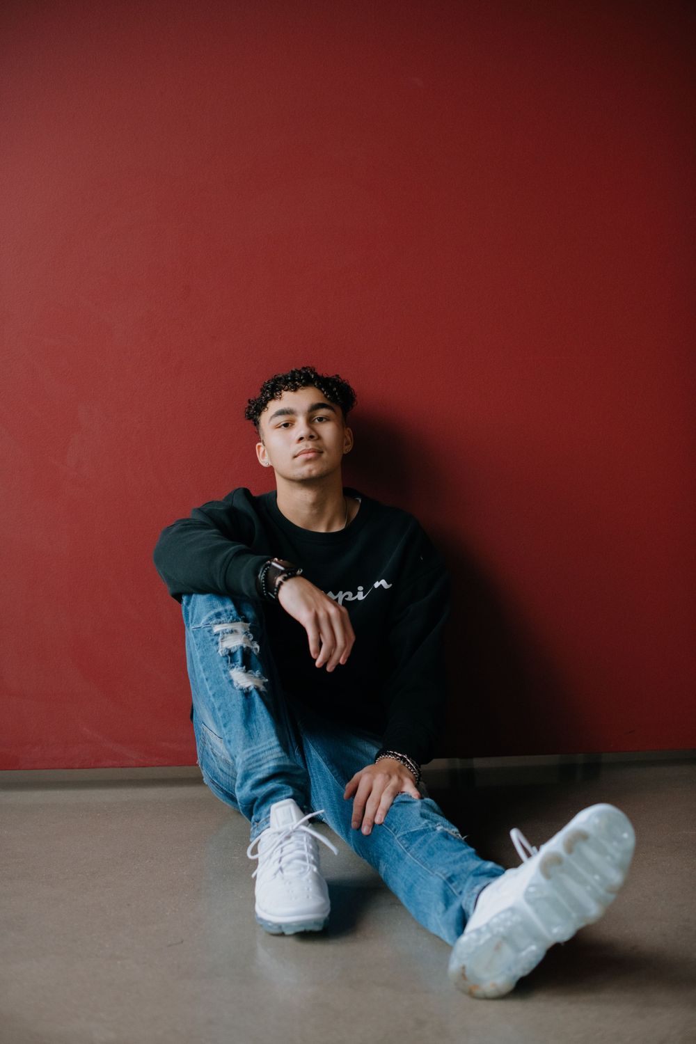 Casual portrait against red wall wearing black sweater and distressed jeans.