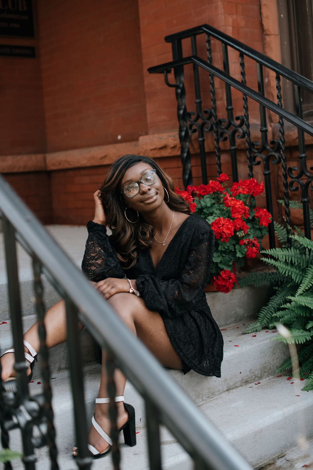 A person sits on red brick steps with blooming red flowers and ornate railings.