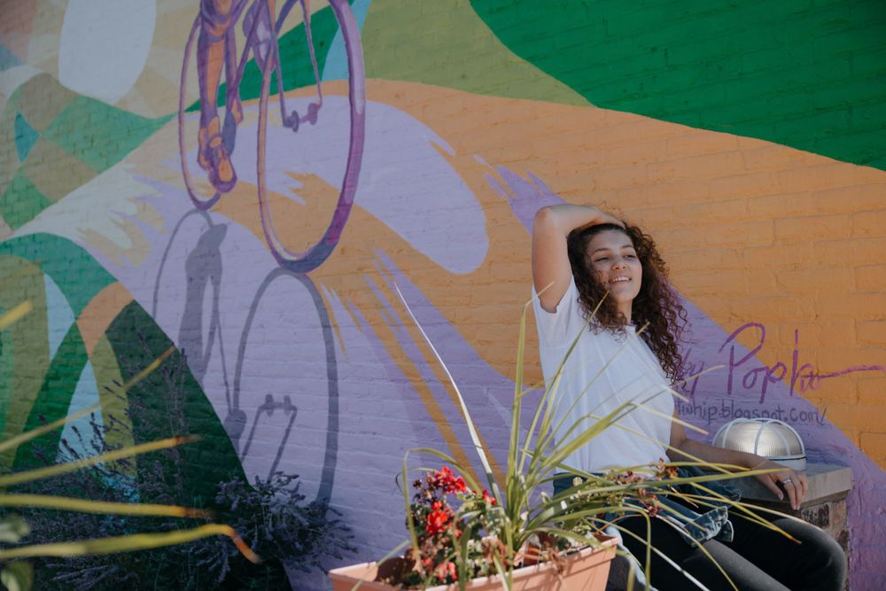 Artistic portrait against pastel mural wall with decorative plants in foreground.