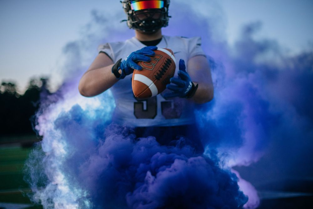 Football player holding ball surrounded by vibrant blue smoke effects.