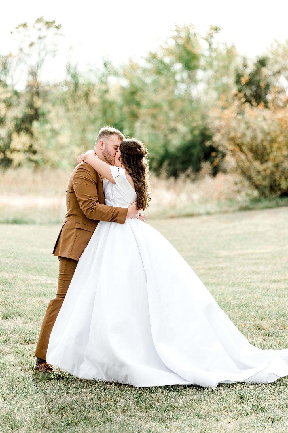 A romantic wedding moment captures a couple embracing outdoors, with the bride in white and groom in brown suit by Stephanie Coulter Photogr