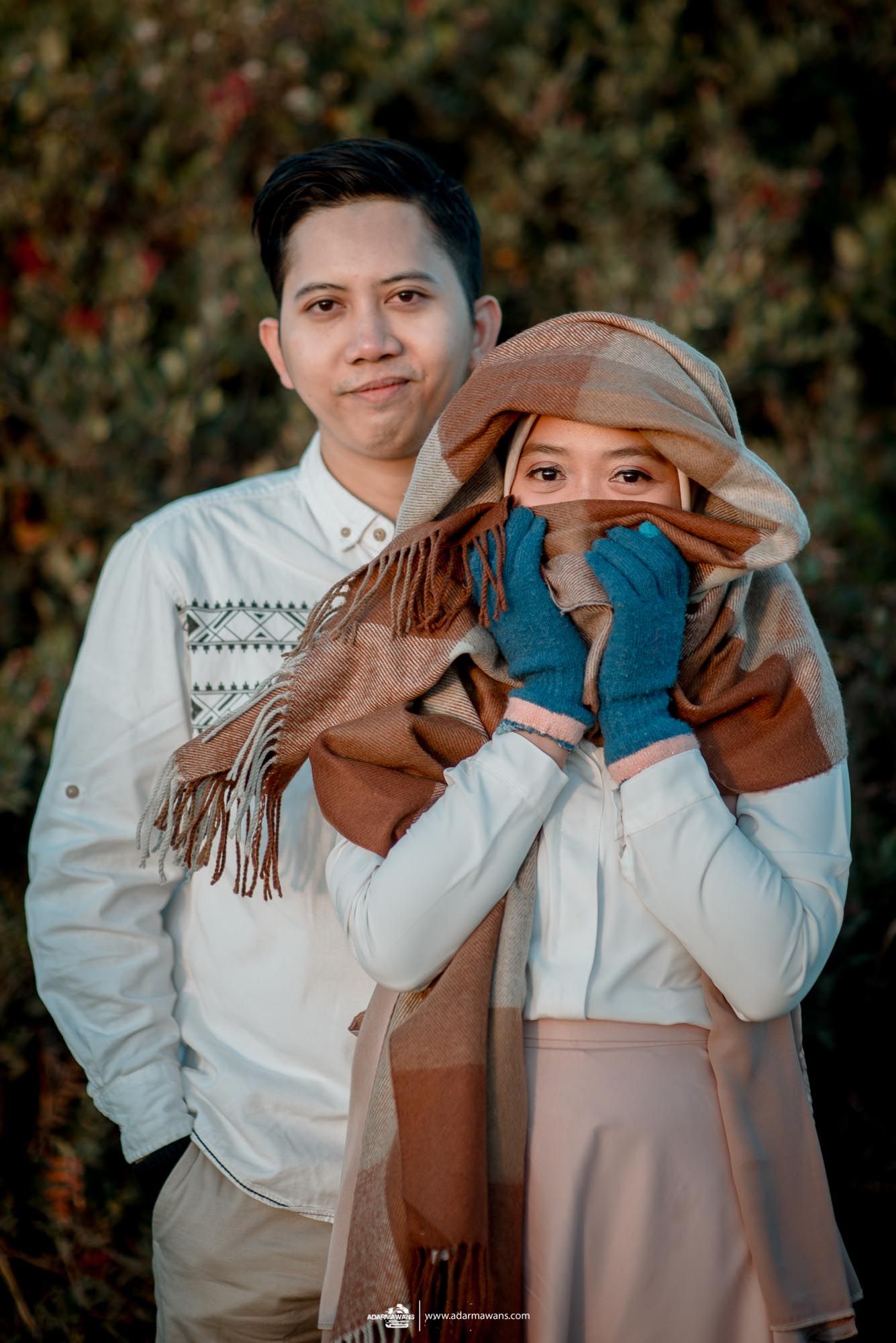 Couple in winter clothing posing together with woman playfully covering her face.