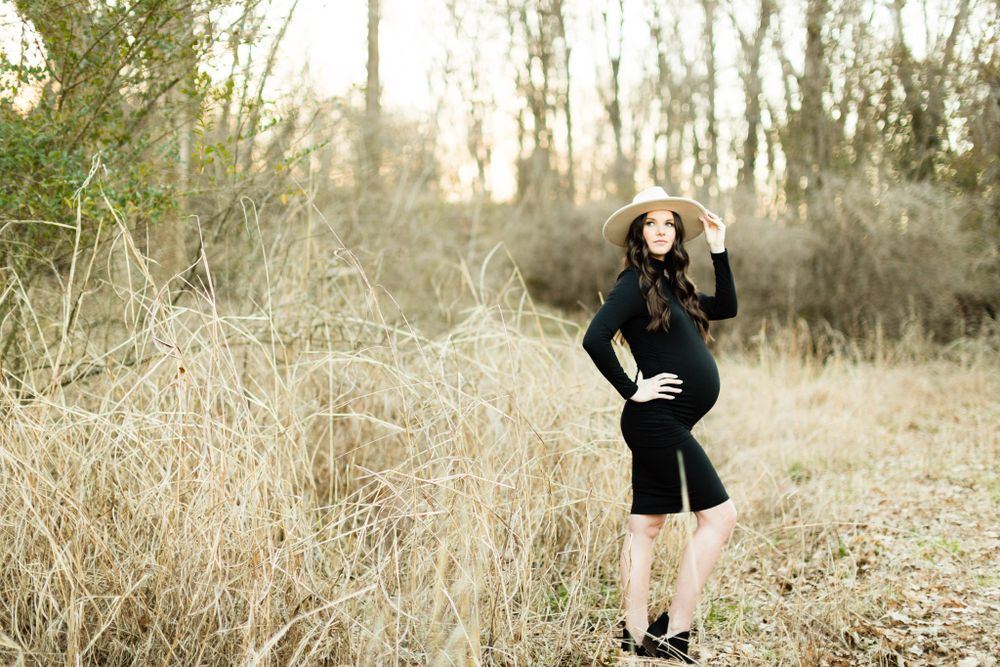 Stylish maternity photo of woman in black dress posing among tall grass.