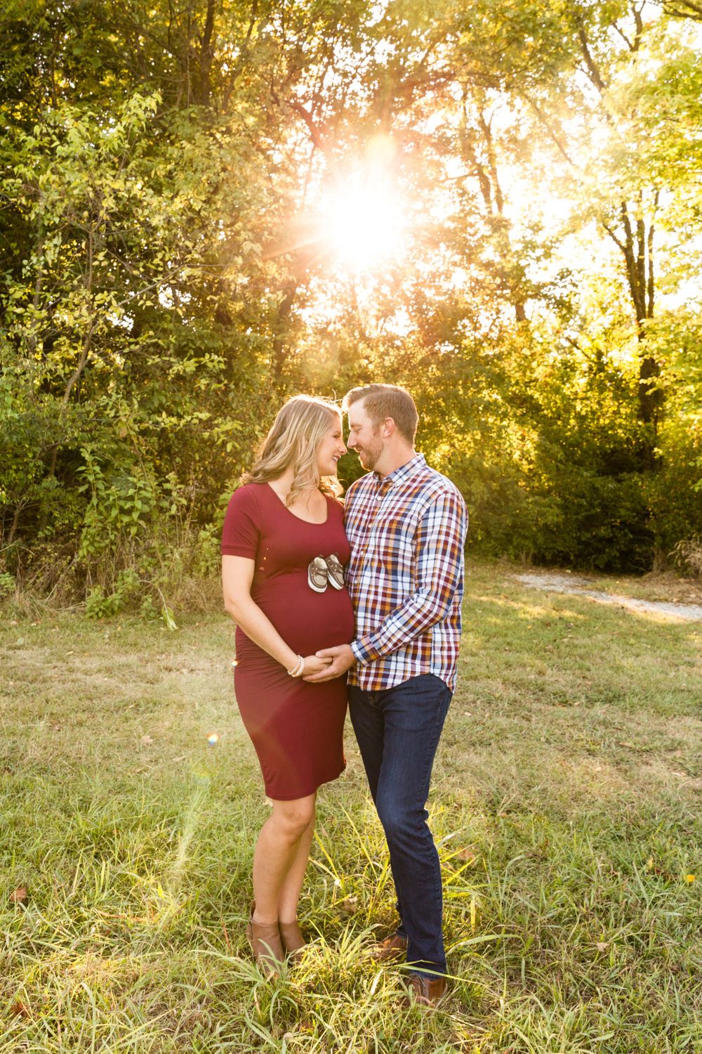 A romantic couple's maternity photo at sunset in a field with glowing sunlight through trees.